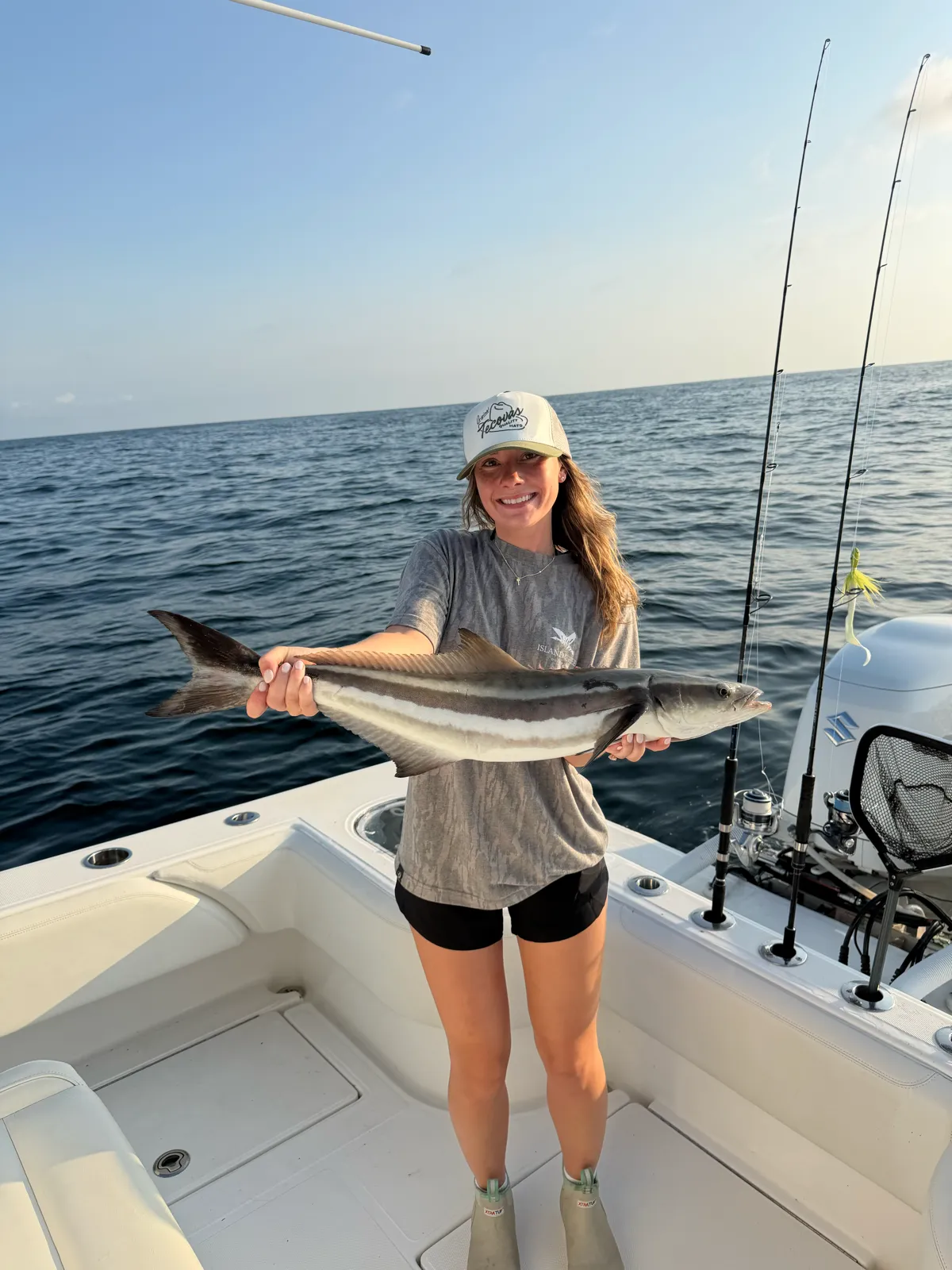 A guest holding a cobia on open offshore water, rods and outboard behind