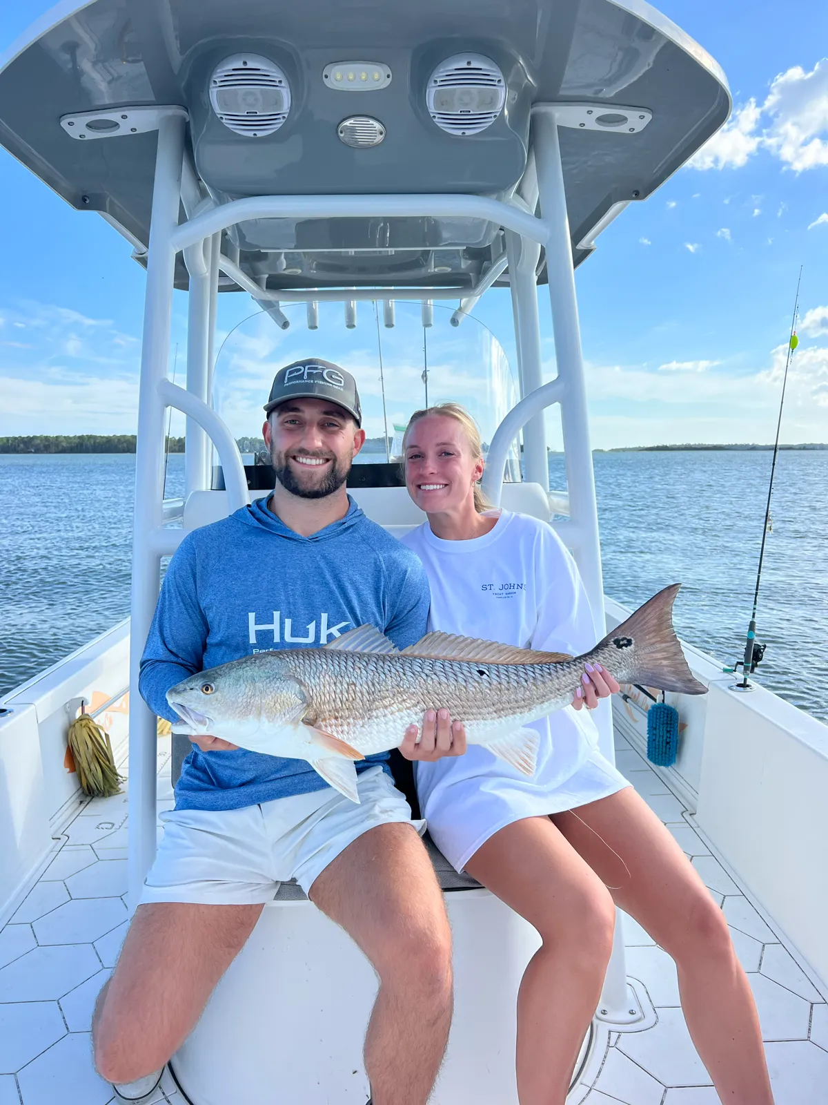 A smiling couple seated under the T-top, holding a big redfish together