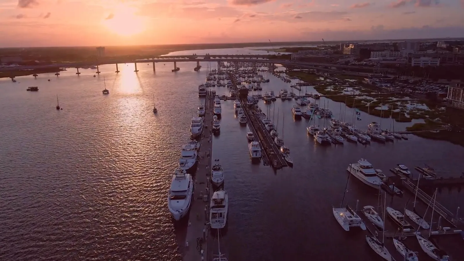 Charleston harbor at dusk from the air, sun low over the bridge and marina