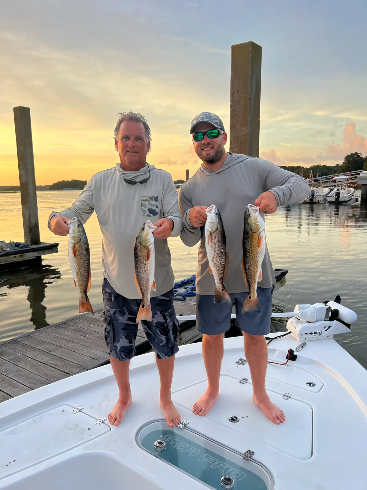 Two guests holding four redfish at sunset on the dock
