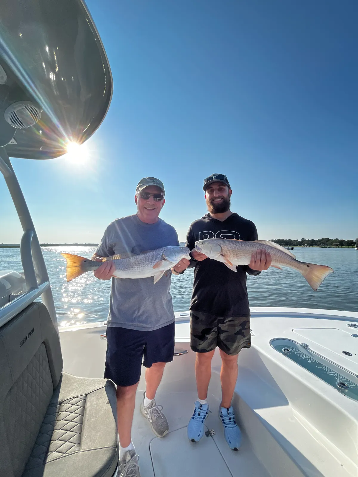 Two guests each holding a redfish as the morning sun flares over the water