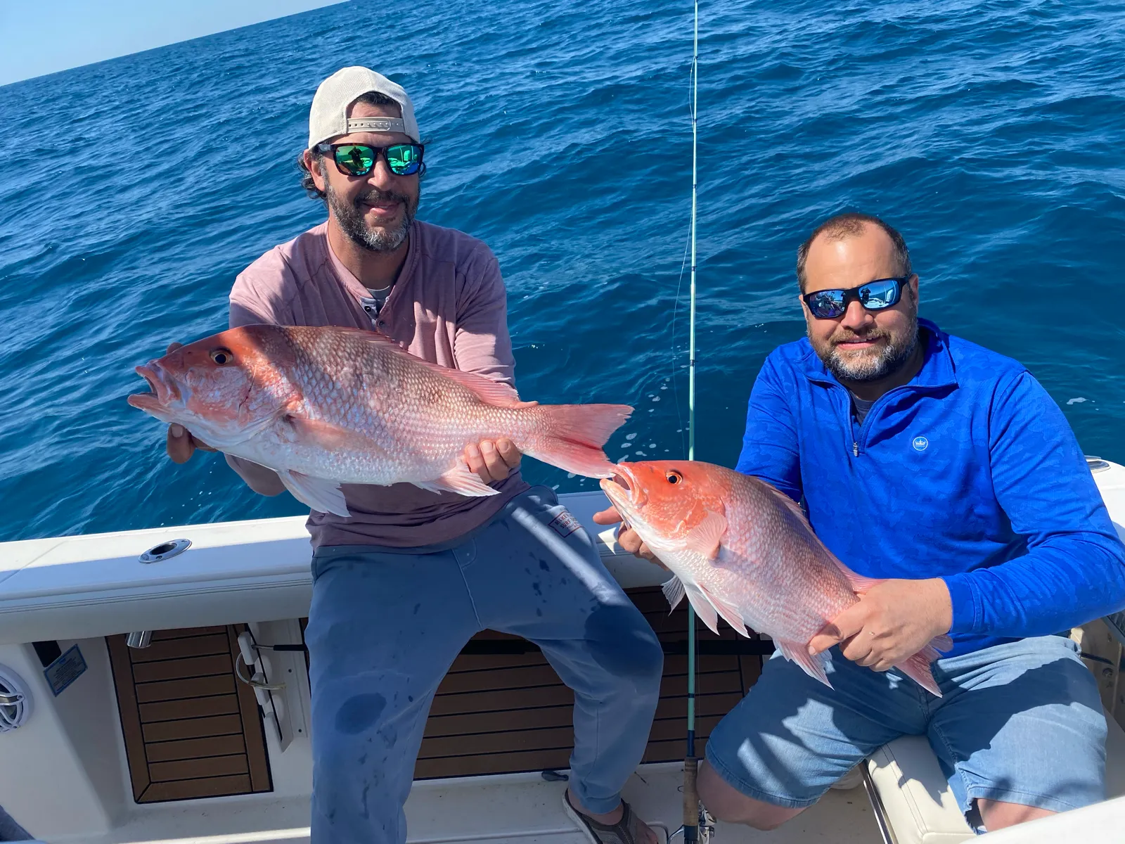 Two guests each holding a red snapper over deep blue water